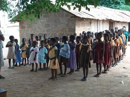 Children lining up outside classrooms at Ghanaian primary school.